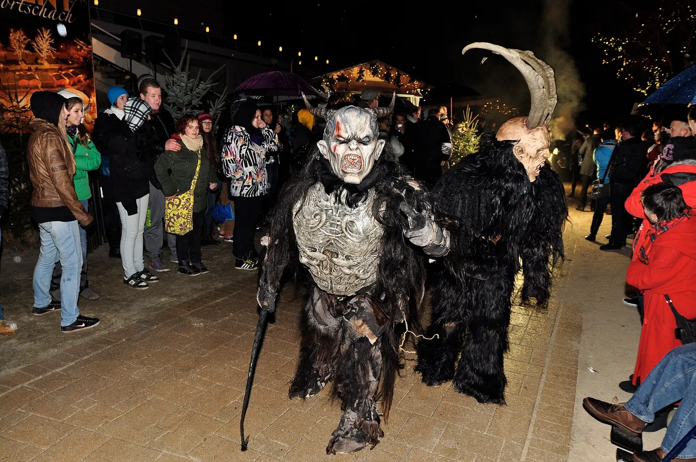 Zwei Krampusse mit Fellkostüm, Hörnern und Masken bei einem Krampuslauf in Kärnten, Zuschauer am Rand