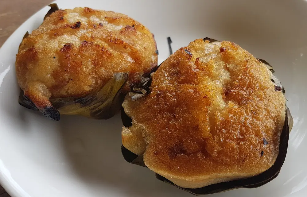 Two bibingka rice cakes in banana-leaf liners with a golden top
