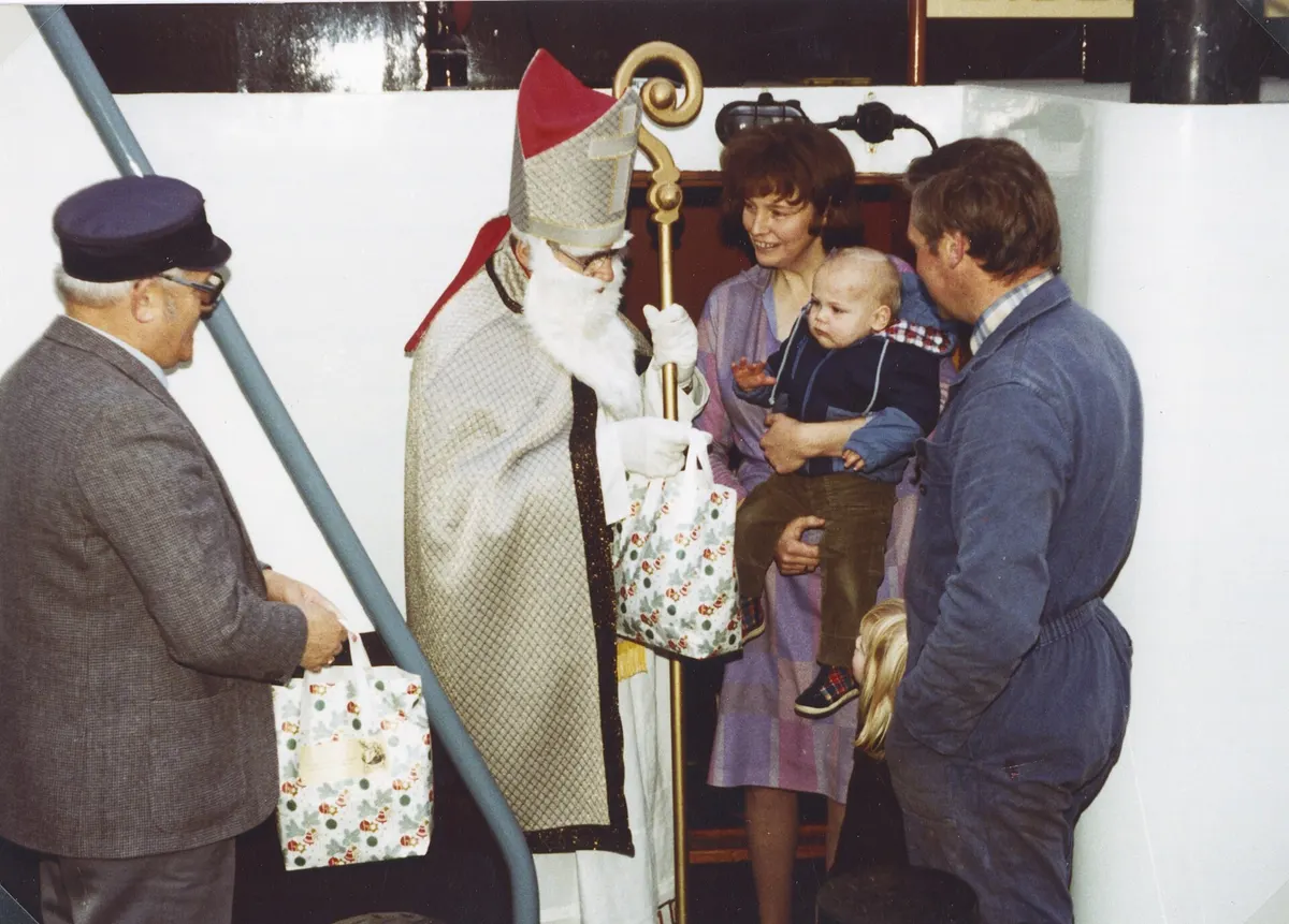 Nikolausbesuch in den 1970er-Jahren: der Nikolaus im Bischofsgewand überreicht einer Familie eine Tüte mit Gaben