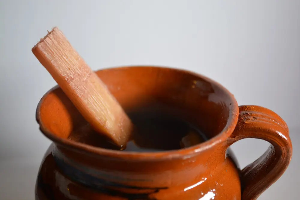 A clay jarrito of hot ponche navideño with a stick of sugarcane