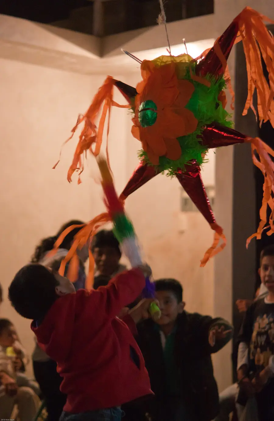 A boy swinging a stick at a star-shaped Christmas piñata at a posada party