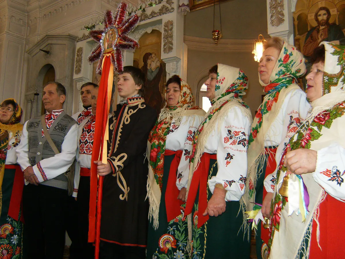 Carollers in embroidered Ukrainian costumes, one holding the Christmas star on a pole, singing in a church