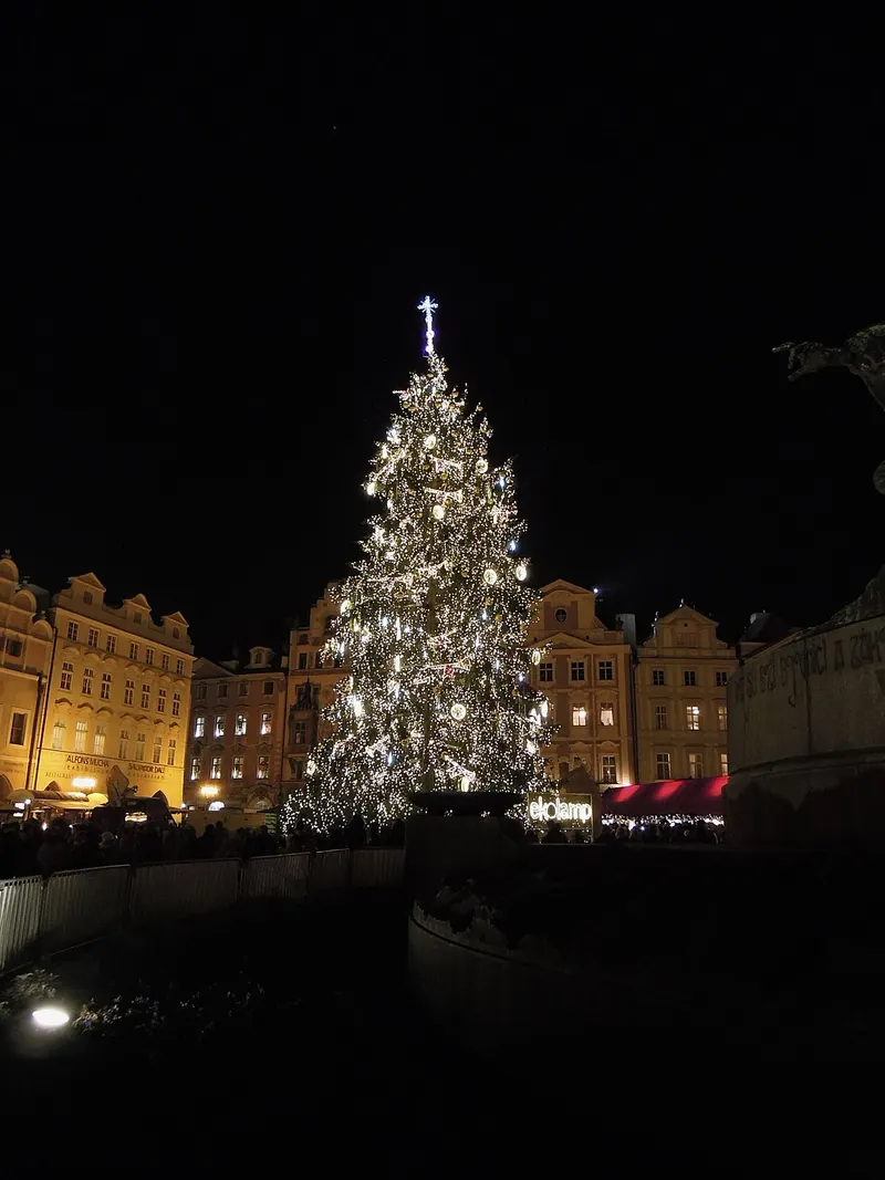 Vánoční strom na Staroměstském náměstí s osvětlenými domy v pozadí
