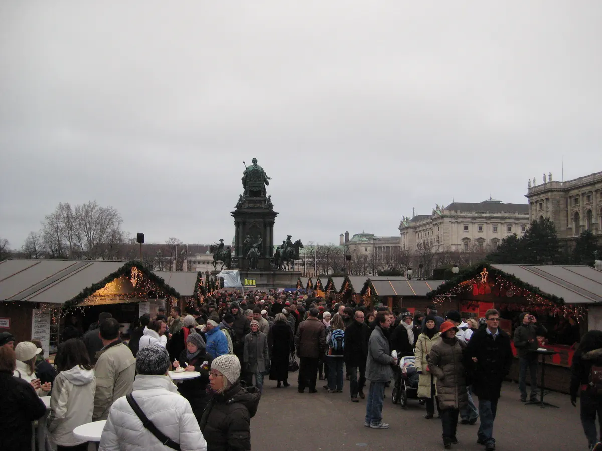 Besucher im Weihnachtsdorf am Maria-Theresien-Platz mit dem Denkmal im Hintergrund
