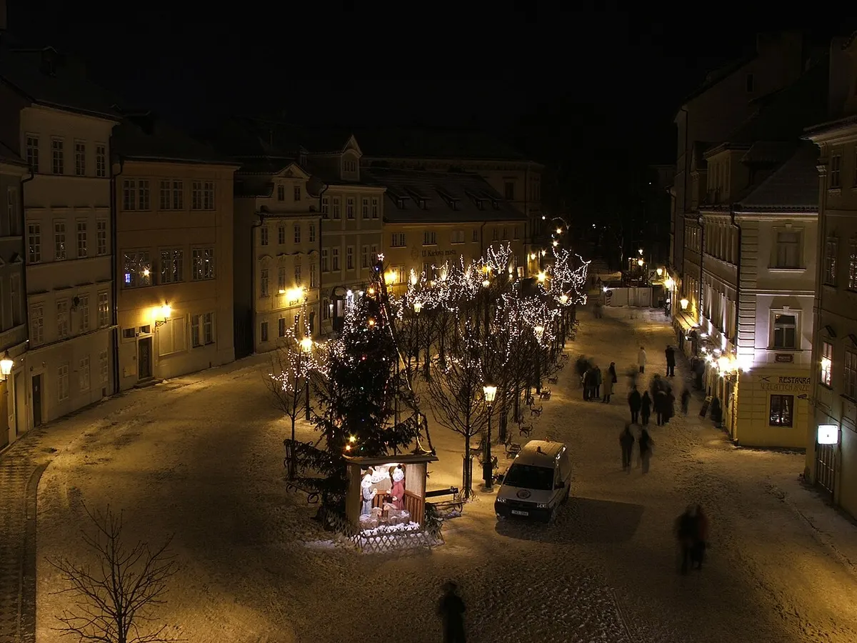Večerní Kampa v Praze s vánočně osvětlenými stromy a stánkem trhu