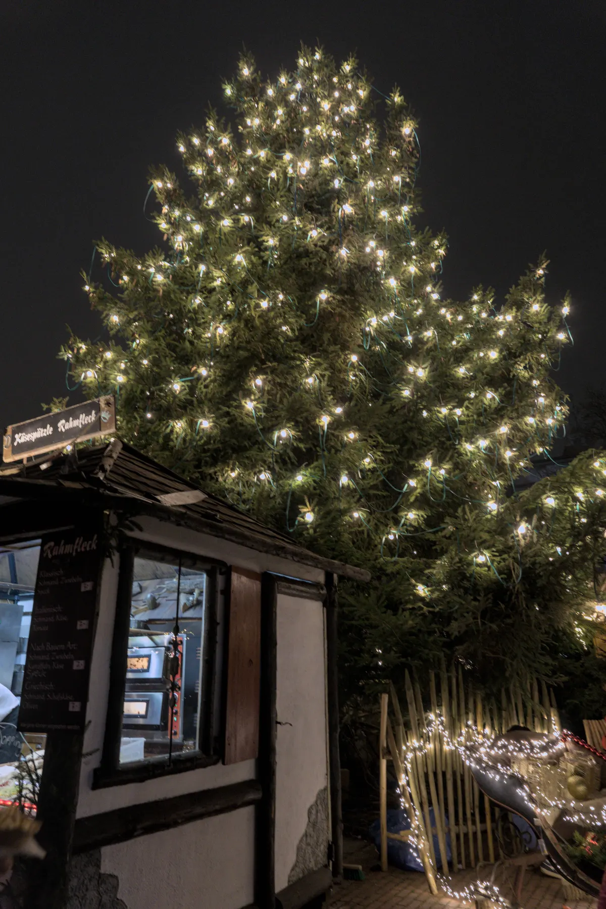 Großer beleuchteter Weihnachtsbaum und Holzhütte auf dem mittelalterlichen Markt Neu-Ulm