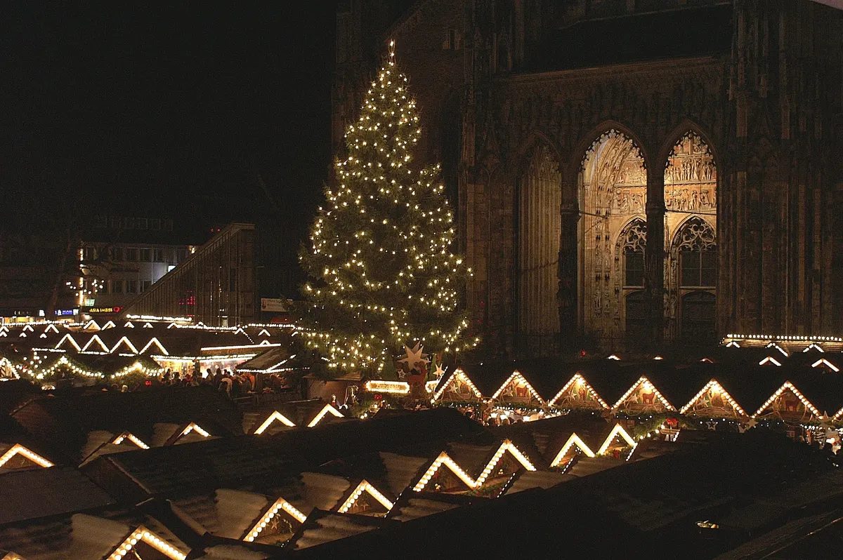 Beleuchteter Weihnachtsbaum vor dem Ulmer Münster über den Buden des Weihnachtsmarkts bei Nacht