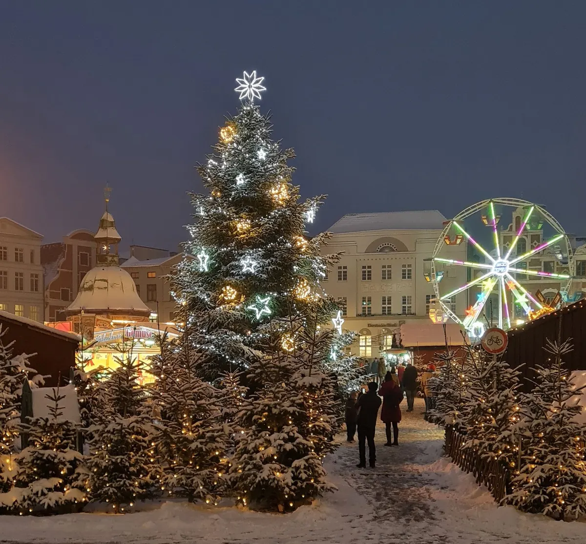 Wismarer Weihnachtsmarkt mit beleuchtetem Tannenbaum und Riesenrad am Abend