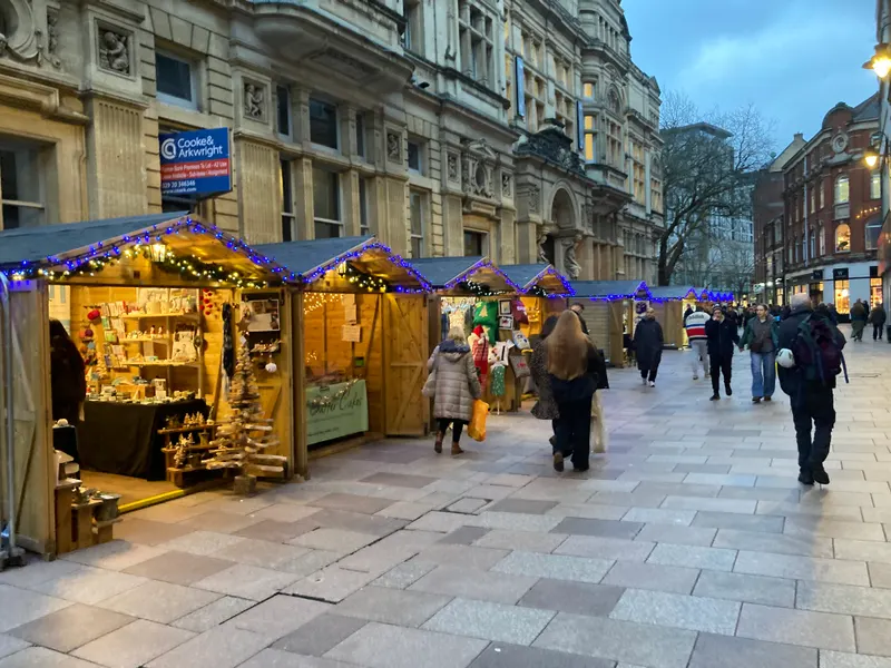 Shoppers at an illuminated Cardiff Christmas Market chalet at dusk