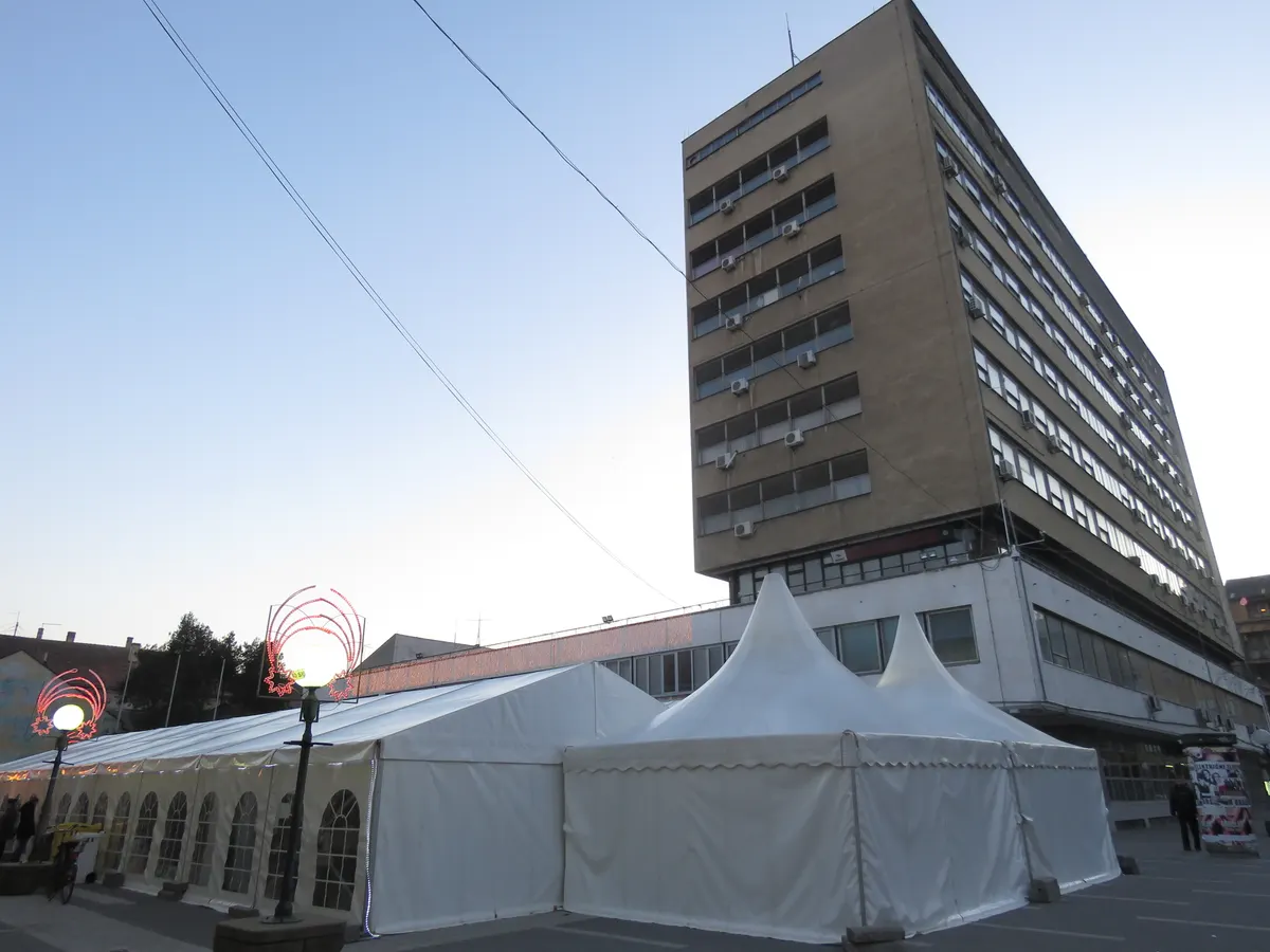 Beli šatori Novogodišnjeg bazara ispred zgrade opštine u Pančevu, sa praznično ukrašenim stubovima