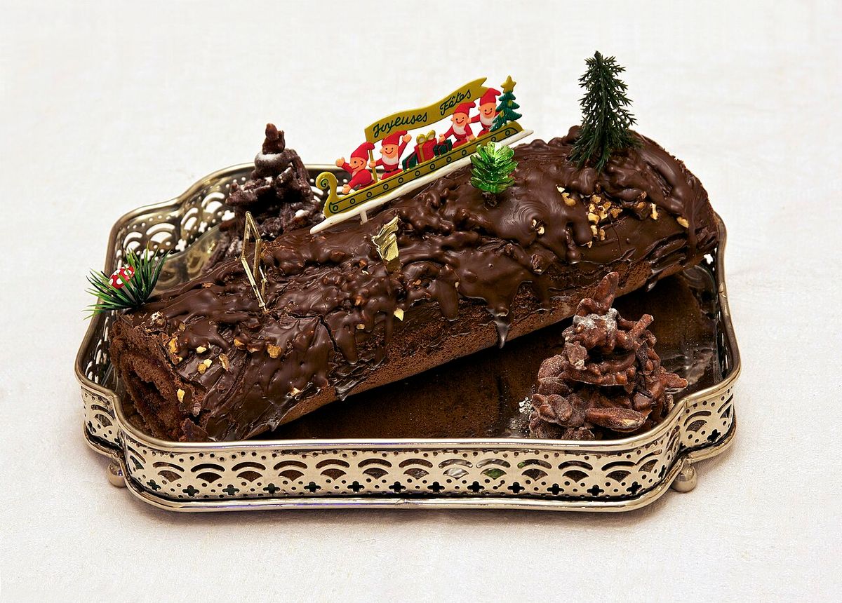 Bûche de Noël au chocolat sur un plateau, avec un décor de sapins et de traîneau