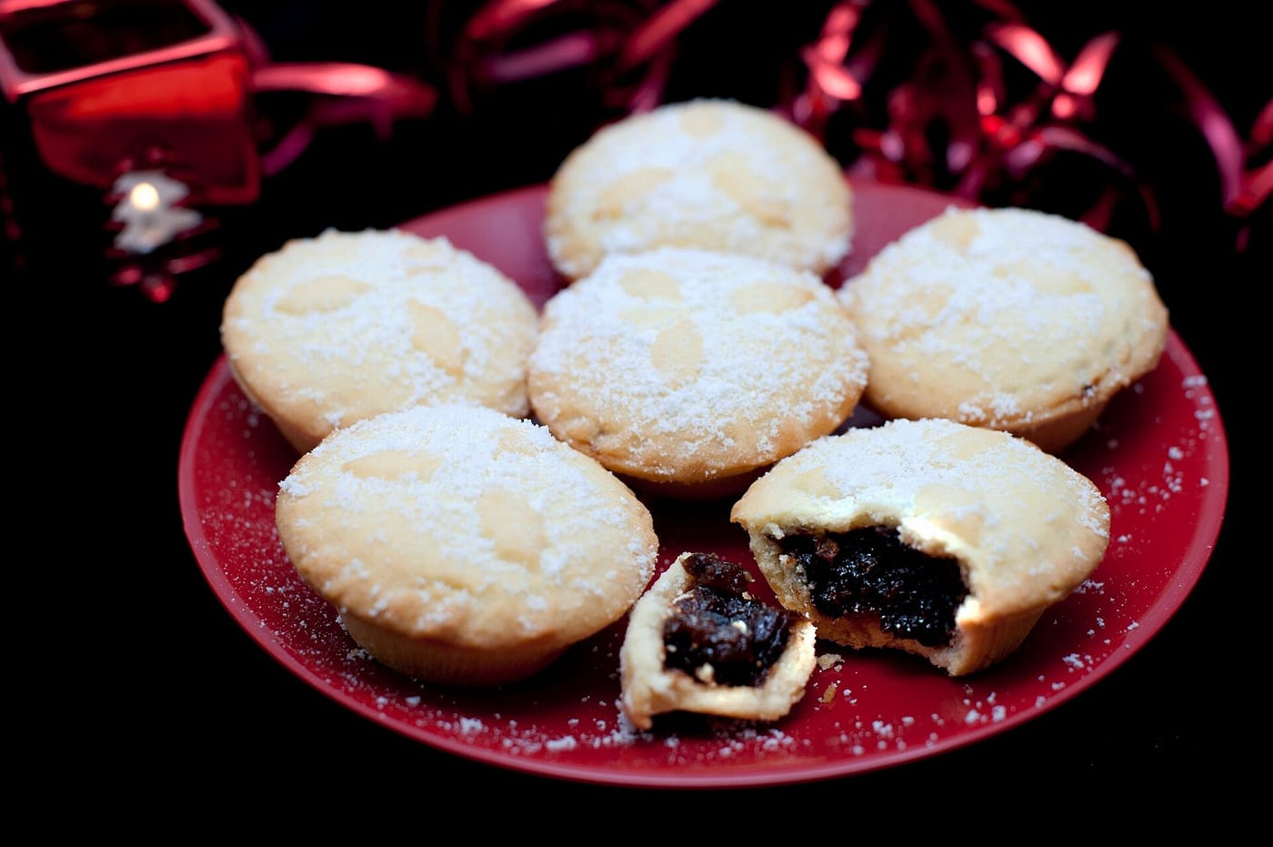 Mince pies dusted with icing sugar on a red plate, one broken open to show the mincemeat
